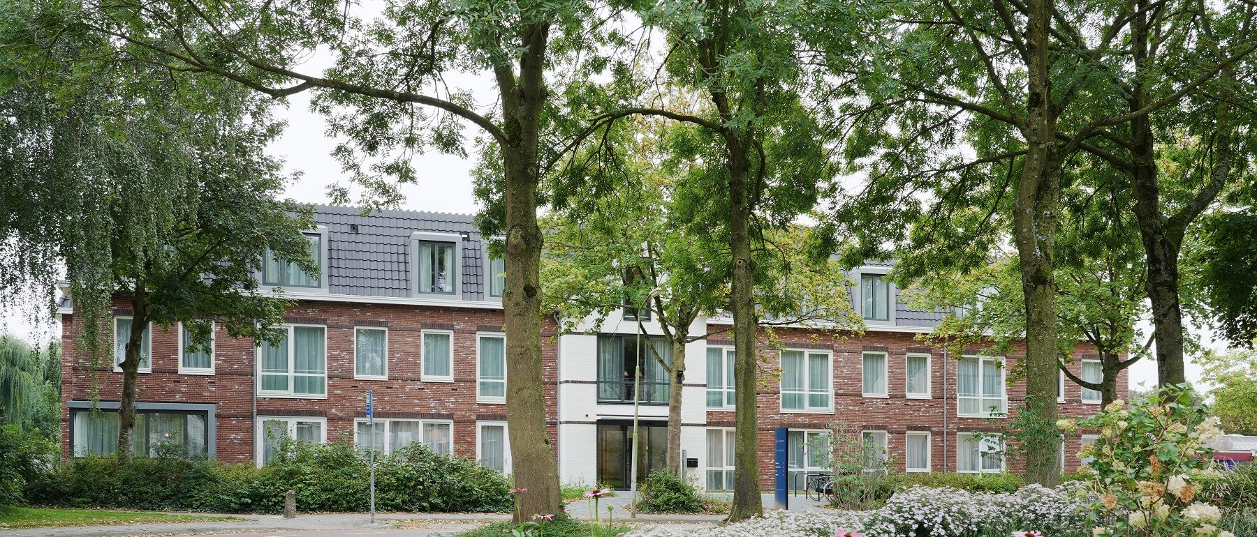 Entree zorglocatie Hof van Waal Tiel met bomen, bloeiende bloemen en groen